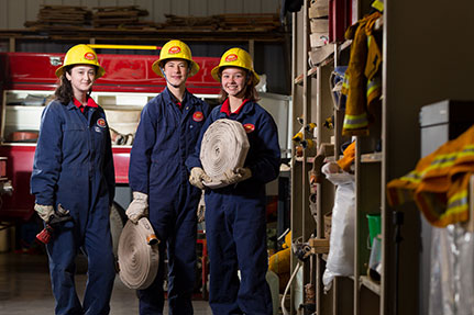 Junior firefighters posing with a water hose and helmet