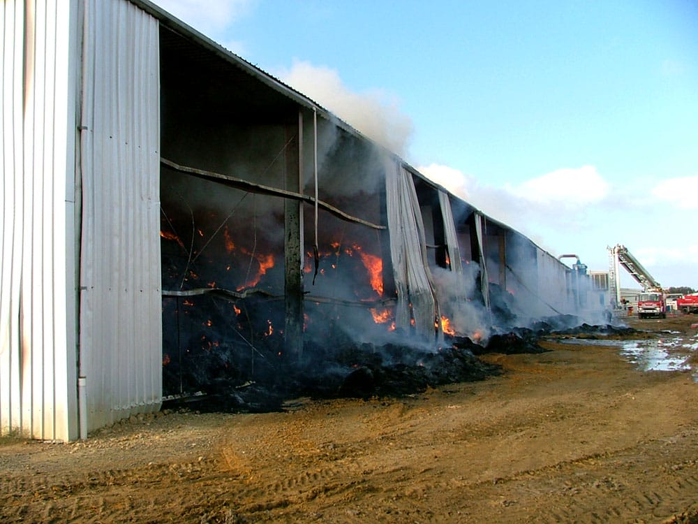 A haystack smouldering in a hay shed which is melting due to fire.