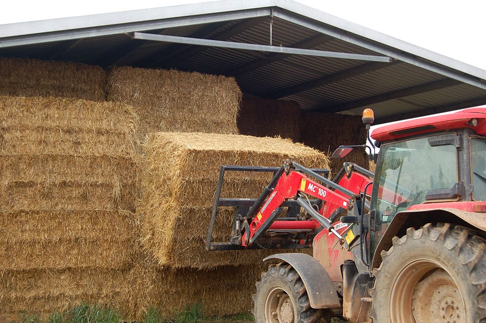 A farmer is using a tractor in a hayshed to pull a haystack apart to stop the bales overheating.