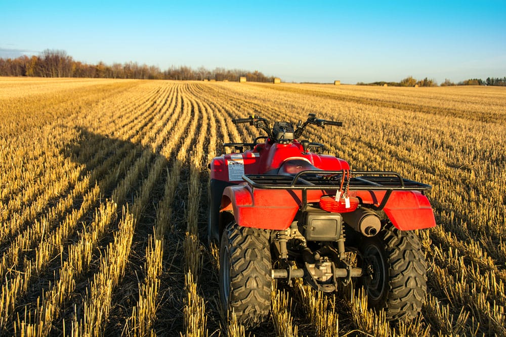A red quadbike parked in a stubble paddock under a clear blue sky.
