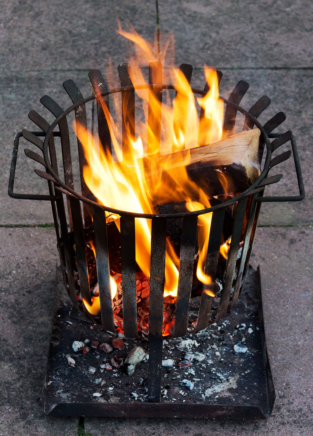 A brazier containing logs on fire sitting on flat stone pavers.