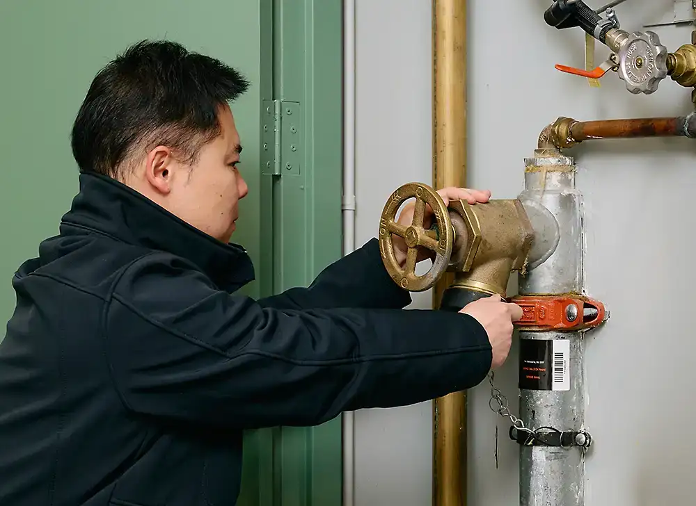 A person wearing navy blue work clothes checking a fire hydrant inside a building.
