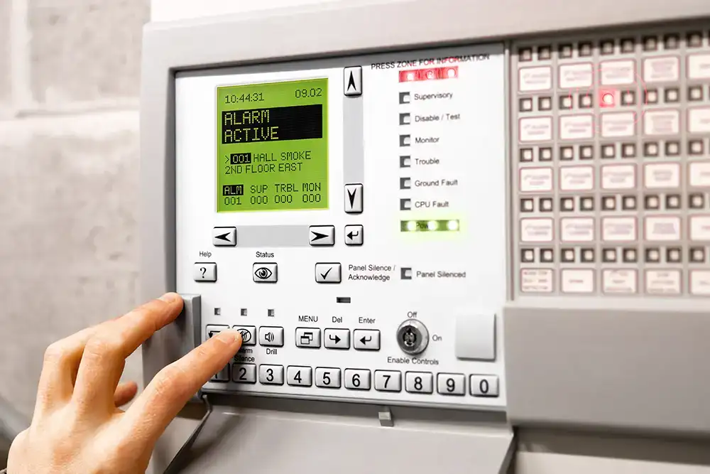A hand pushing a button on a commercial fire indicator panel which is in alarm mode