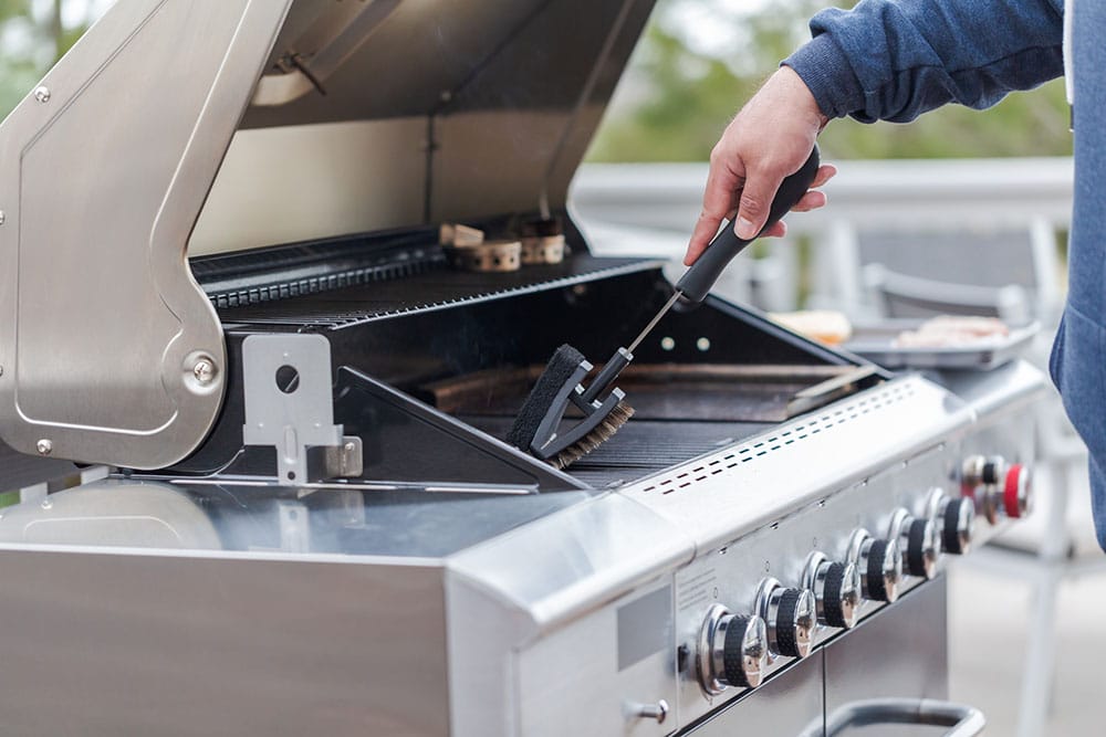 A person cleaning a BBQ grill with a brush.