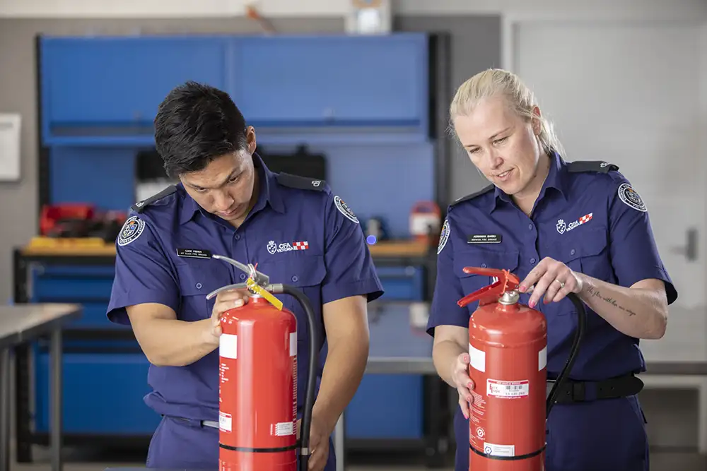 Two volunteer fire brigade members are inspecting fire extinguishers in a workshop.