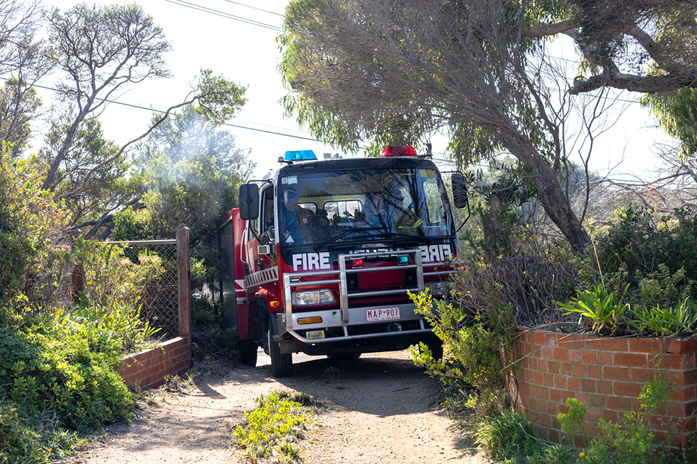 Fire truck attempting to drive through a property gate with fence post, retaining wall and bushes either side making access difficult.