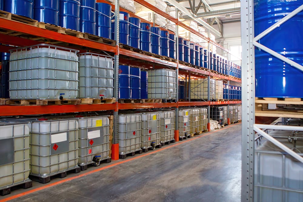 Spacious warehouse with rows of stacked blue barrels and white containers on metal shelves to highlight a organised industrial setting.