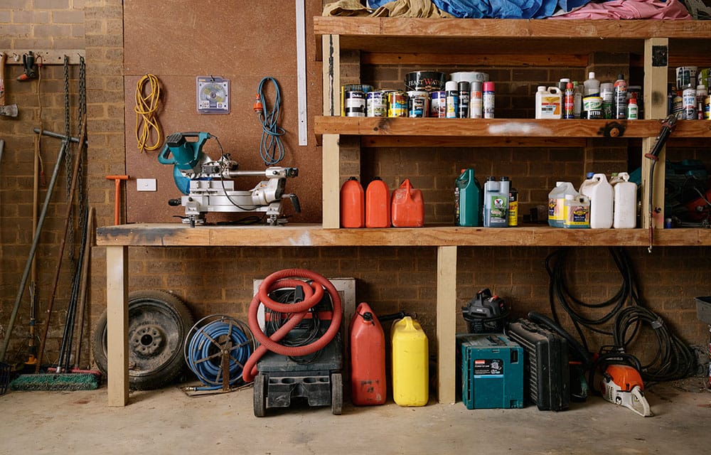 Assorted fuels, oils, paints and other chemicals stored neatly and separately on shelves in a garage.