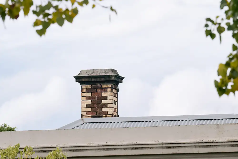 A brick chimney standing from the tin roof of a house.