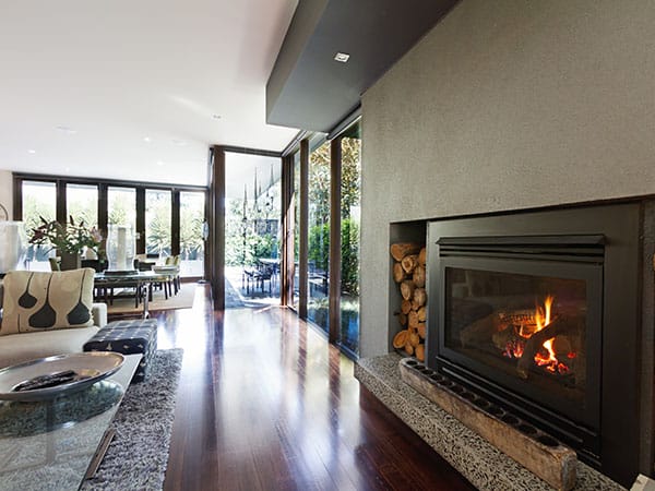 Wood heater in a modern living room that has polished wooden floor, and glass doors leading to outside patio.