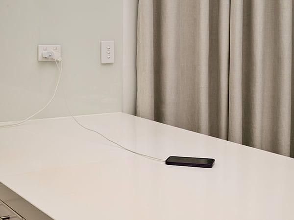 A mobile phone charging on a white stone kitchen bench top. Curtains are closed in the background.