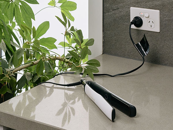 Hair straightener resting on a stone bench top and plugged into a power point in a bathroom.
