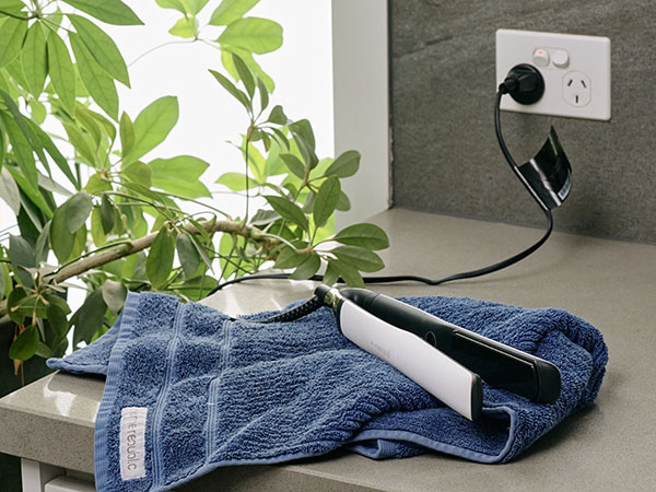 Hair straightener resting on a blue towel on top of a stone bench top. plugged into a power point in a bathroom.