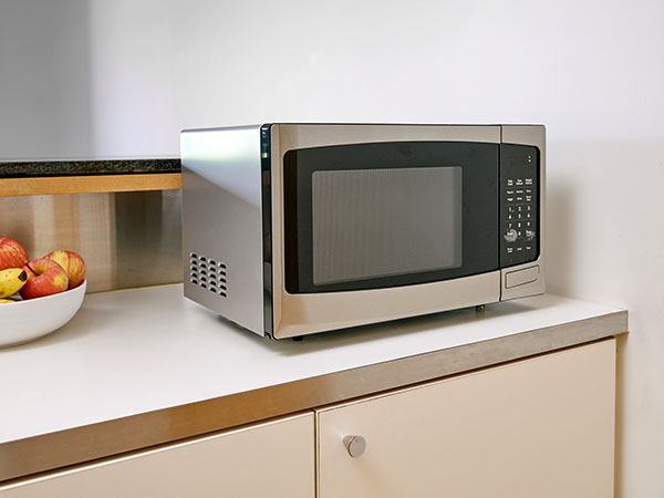 Microwave on a kitchen bench top next to a fruit bowl.