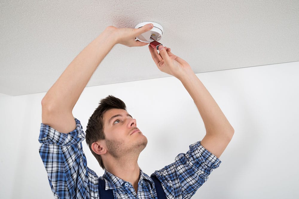 A person replacing a battery in a ceiling-mounted smoke alarm.