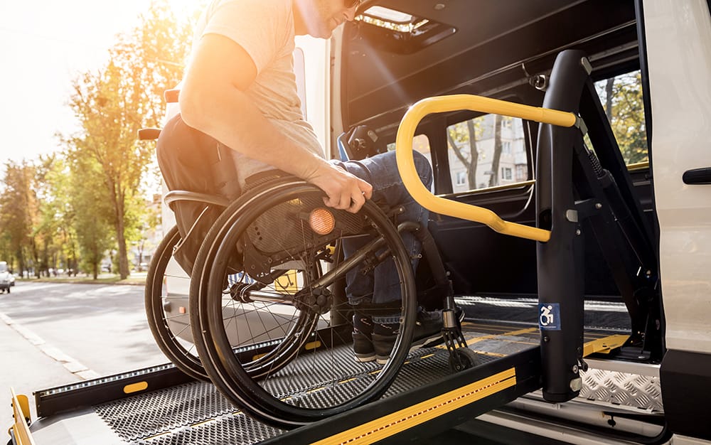 A man in a wheelchair is boarding a bus on a sunny day. He is using a ramp designed for passengers who use a wheelchair or mobility device.