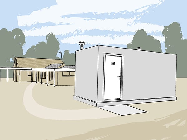A bunker above the ground, standing next to a house. It is a rectangular building with two vents in the roof. 