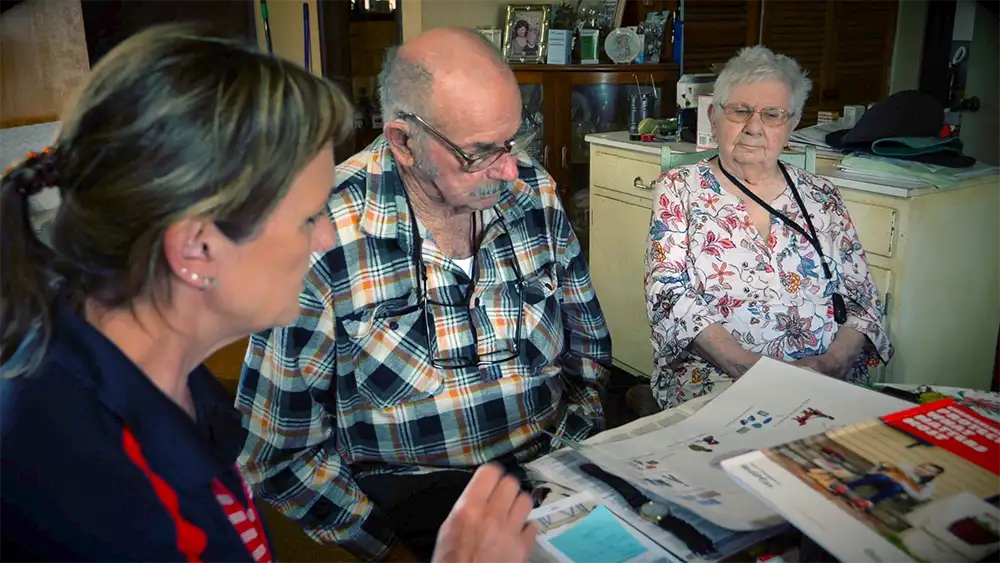 A CFA volunteer and an older couple are sitting at a table looking at bushfire plan documents. 