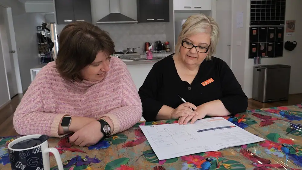 A carer is sitting with their middle aged client looking at the home fire safety escape plan template. 