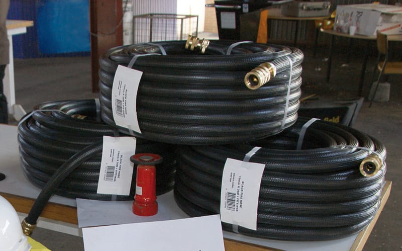 Three large coils of black fire fighting hose with brass fittings, stacked in a pyramid along with a red fire fighting nozzle.