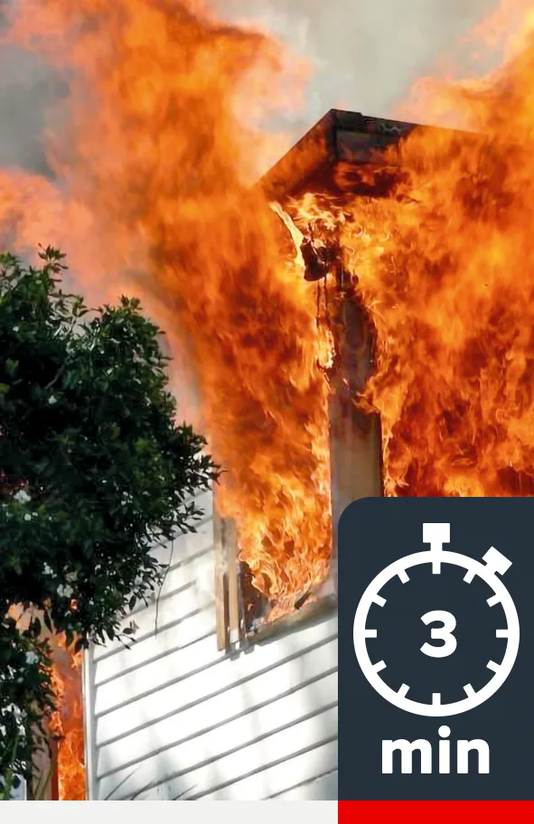 Looking from outside, flames are roaring out through the windows of a house.