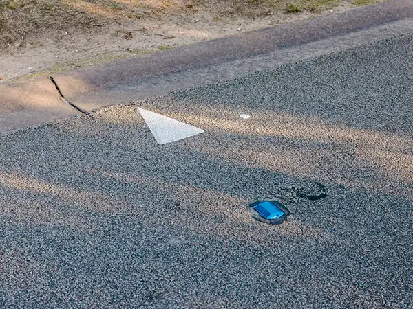 A blue catseye reflective marker embedded in the road surface next to a white painted triangle.